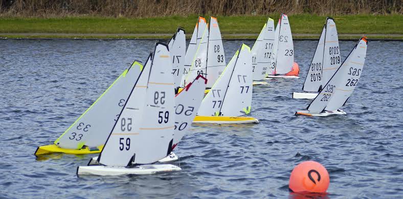 A yellow hulled radio controlled sailboat heeling upwind in bright sun