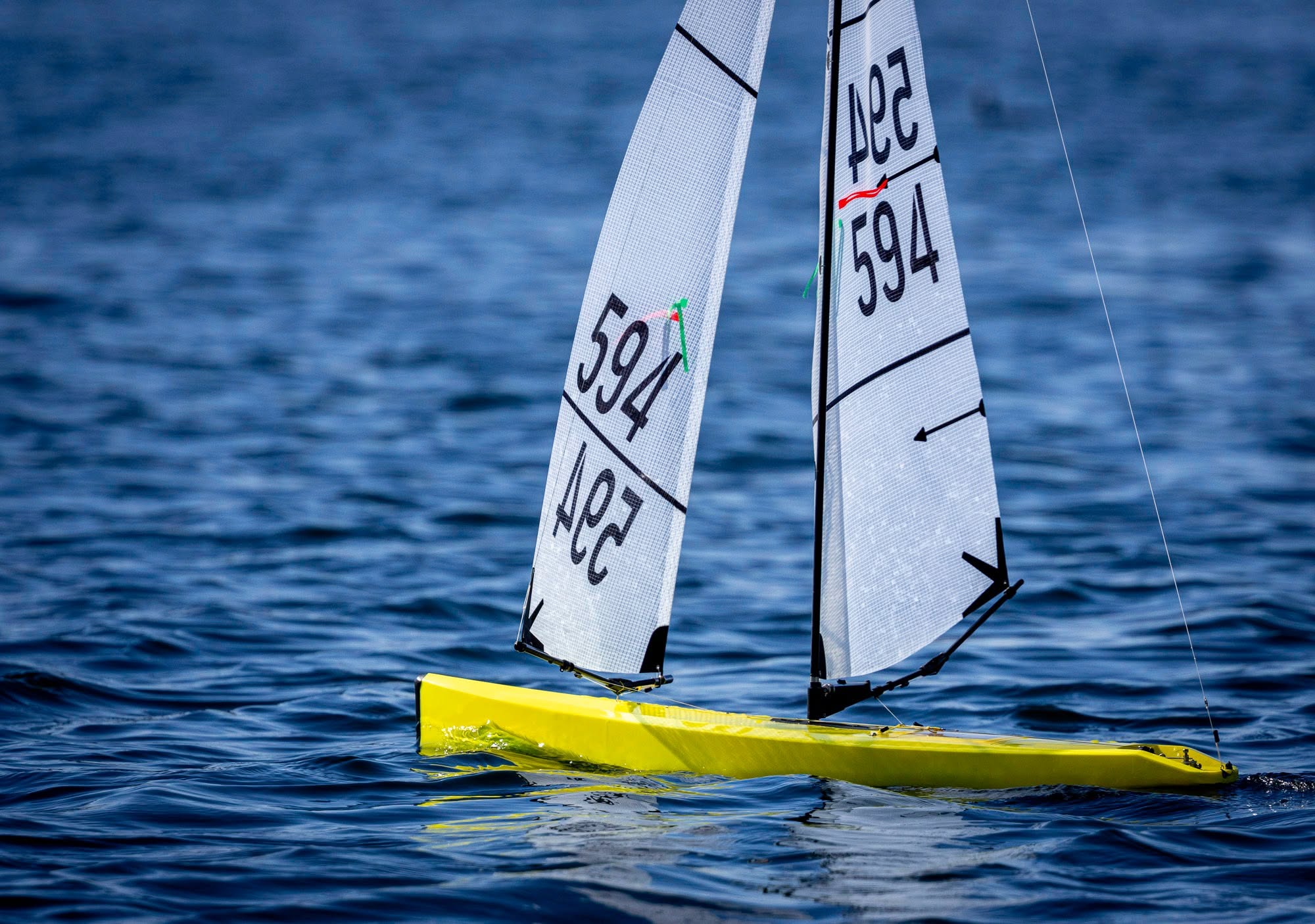 Two radio controlled sailboats side by side on the water with sails trimmed for a reach